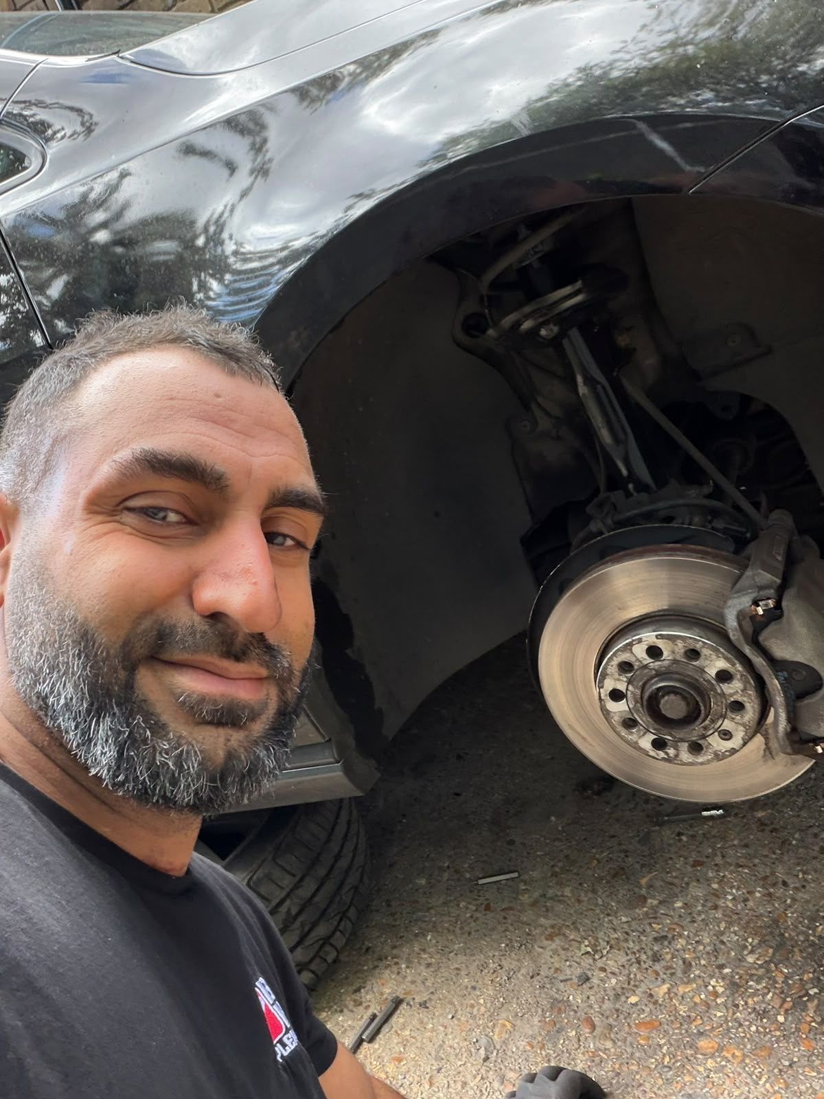 Max, the mechanic behind MaxFix Auto, beside a car with the front brake exposed