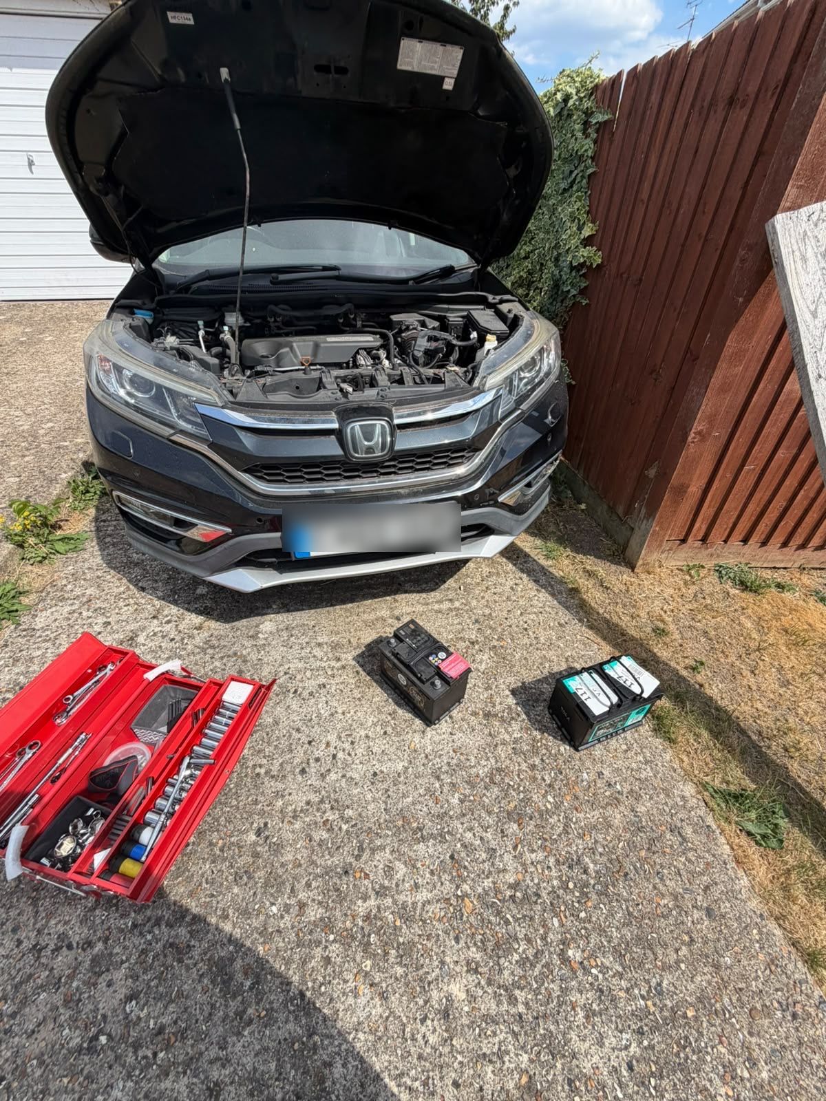 Old and new car batteries beside a Honda CR-V with the bonnet open