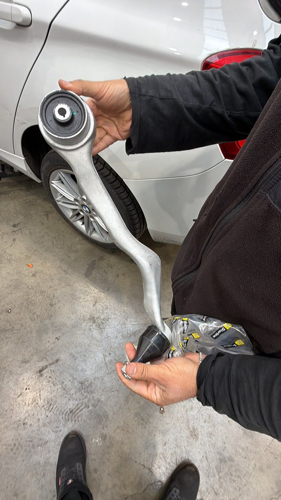 Replacement BMW suspension control arm held beside the vehicle